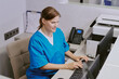 © AnnaStills - Caucasian middle aged woman wearing medical scrubs working at computer in modern office setting, sitting at desk and typing on keyboard with printer and phone visible in background
