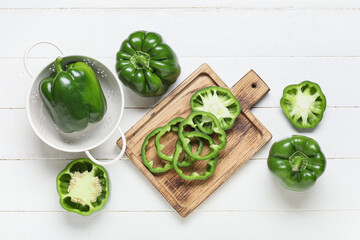 Wall Mural - cutting board and colander with green bell peppers on white wooden background