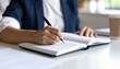 © Nopadon - A person is writing in a notebook with a pen, seated at a table with papers and a coffee cup nearby, suggesting a productive work or study session.