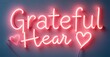 © antishock - Bright neon sign displays words Grateful Hear with heart symbols. Pink glow dominates dark background. Simple, modern aesthetic.