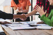© Wasan - Business partners shaking hands at a meeting while their coworkers are clapping, celebrating the closing of a deal or a successful agreement.
