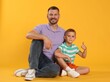 © New Africa - Happy father and son showing thumbs up on yellow background