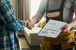 © pressmaster - Caucasian middle aged man wearing tool belt holding invoice clipboard shaking hands with unseen young adult Caucasian woman in home interior, confirming service completion