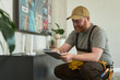 © pressmaster - Caucasian middle aged man with beard wearing cap setting up wireless router using digital tablet in modern living room, focusing on configuring home internet connection
