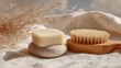 © Ahmad - A bar of soap rests on a light-colored stone, next to a wooden body brush, all set on a beige fabric backdrop with dried pampas grass.  The scene is softly lit, creating a calm and natural aesthetic