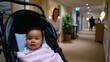 © Milos - A cute baby relaxes comfortably in a stroller while caregivers approach, capturing the essence of attentive parenting in a warm and inviting hotel corridor environment.