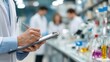 © Justlight - Medium shot of researcher writing notes on clipboard blurred colleagues and lab glassware behind emphasizing clinical trial documentation.