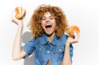 © VICHIZH - Happy young woman with curly hair holding two burgers against a white background, celebrating delicious food with excitement and joy