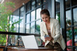 © Crystal - Young asian businesswoman comparing information on her laptop and smartphone while working remotely at an outdoor cafe, enjoying the pleasant atmosphere