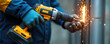 © Viktor - Construction worker in blue, yellow uniform wears protective gloves, holding yellow cordless drill. Tool creates sparks as works on metal, signifying skill, power, industrial effort. Close-up detail