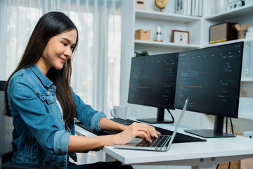 Smiling young Asian in IT developer creating with typing online information on laptop with coding program data of application, wearing jeans shirt. surrounded by safety analysis two screen. Stratagem.