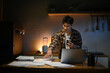 © Stella 16 - Focused man working late at night on laptop in kitchen with coffee