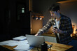 © Stella 16 - Young man sits in the kitchen at the bar counter works in laptop and drinks a coffee. Home atmosphere, work in the evening after a hard day. Home office.