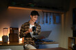 © Stella 16 - Young man sits in the kitchen at the bar counter works in laptop and drinks a coffee. Home atmosphere, work in the evening after a hard day. Home office.