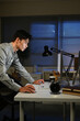 © Stella 16 - A man is stand at a desk at night with a computer and a keyboard. He is looking at the computer screen