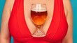 © master1305 - Close up of beer glass placed in red dress cleavage on blue background. Concept of Oktoberfest humor, playful lifestyle, beverage creativity, bold advertising, and festive cultural expression.