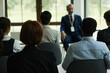 © DragonImages - Group of young and middle aged multiethnic professionals listening to Caucasian senior man speaking at business seminar, all seated in conference room facing presenter