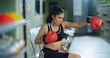 © Raushan_films - Indian young adult gen z sports woman lady sitting on chair do practice boxing Asian angry girl wear gloves hand in air learn beating inside hall way place campus