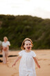 © Austockphoto - Young girl in white dress running on sandy beach at sunset while family walks behind her