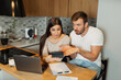 © Novak - Couple checking bills at home with calculator and laptop, managing family finances and expenses together