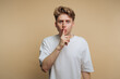 © bodnarphoto - Young man making a shushing gesture against a plain background while maintaining an intense expression