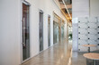 © TrueFrame Collective - Modern office hallway featuring glass doors along walls, polished concrete floor reflecting light, row of numbered lockers on right side, empty corridor extending into distance