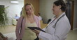 © Marco - Female doctor reviewing medical details on tablet with woman in reception area of clinic, positive healthcare conversation near waiting area