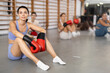 © JackF - Positive young girl wearing boxing gloves sitting on the floor in sports hall with others