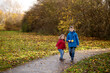 © Tatjana - Brother and sister walking on park path surrounded by golden autumn leaves.