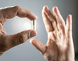 © SERIGALA MALAYA - Pill between fingers: A detailed shot showcases a close-up of a hand delicately holding a single, pristine pill against an open palm, evoking themes of medicine, health, and wellbeing.