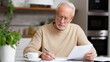© Curioso.Photography - Senior man sitting at table and reading documents in a cozy home environment.