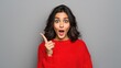 © Johannes - amazed young happy indian girl student lady shopper professional excited face looking at camera pointing finger at copy space surprised by shopping sale offer isolated on gray studio background no lo