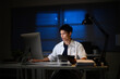 © Prathankarnpap - Male office worker reviewing reports and data under desk lamp in dark workplace