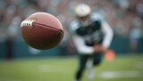 Close-up of a football flying through the air. In the background, a blurred player runs on the field. The ball is in focus, creating a sense of dynamic motion.