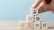 © Cheewynn - Wooden blocks with business icons are stacked in a pyramid, symbolizing leadership, strategy, and growth, with a hand placing the top block