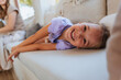 © bernardbodo - Smiling little girl lying on sofa with her mother in the background