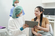 © Ekkasit A Siam - Asian dentist wearing surgical gown and mask showing digital x-ray to female patient using tablet in dental chair, discussing treatment plan with nurse assistant standing nearby in dental clinic
