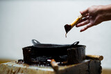 Close up of artisan hands using canting tool filled with hot wax to draw patterns on fabric, traditional Indonesian batik making process with smoke rising from the tool.