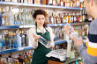 © JackF - Woman works as salesperson in alcohol department of Russian store and recommends high-quality vodka to unrecognizable man buyer, shows assortment