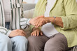 © Pixel-Shot - Young woman with grandmother holding hands at home, closeup. Care concept