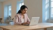 © DWIJ - Young indian woman wearing glasses working on a laptop at a wooden desk in a bright office