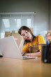 © Witoon - A young Asian businesswoman sits stressed at her desk, managing online orders, shipping boxes, facing retail challenges, worry, and frustration.