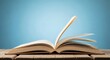 © Farhan - A single page of an open book is caught in motion on a wooden desk, against a solid blue studio background. Represents the flow of a story or turning a new chapter.