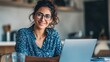 © Johannes - smiling indian young adult woman wearing glasses typing on laptop computer working at home office sitting at table happy female professional freelancer student studying online using notebook pc no lo