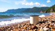 © Joko - Beige mug rests on a rocky beach with ocean waves and distant mountains