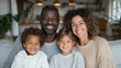 © Sergio IQstock - A cheerful mixed-race family enjoying time together at home, parents and children sitting on the sofa, bright natural light in a cozy modern interior. multicultural family, diverse