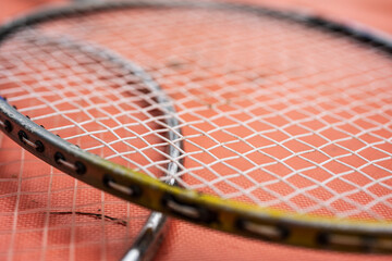 Old badminton rackets overlapping on orange surface.