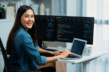 Young Asian in IT developer looking at camera to present with online information on pc with coding program data application, wearing jeans shirt. surround by safety analysis two screens. Stratagem.