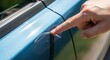 © Chainarong - A man's hand carefully points to a recent scratch on the blue paintwork of a modern vehicle door