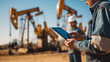 © PACHARA - A man is holding a tablet in front of a large oil rig